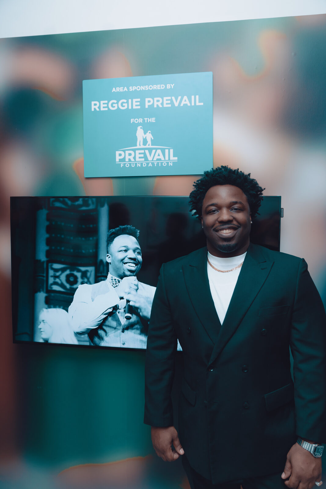 Reggie Prevail beside the sign reading Area Sponsored by Reggie Prevail for the Prevail Foundation